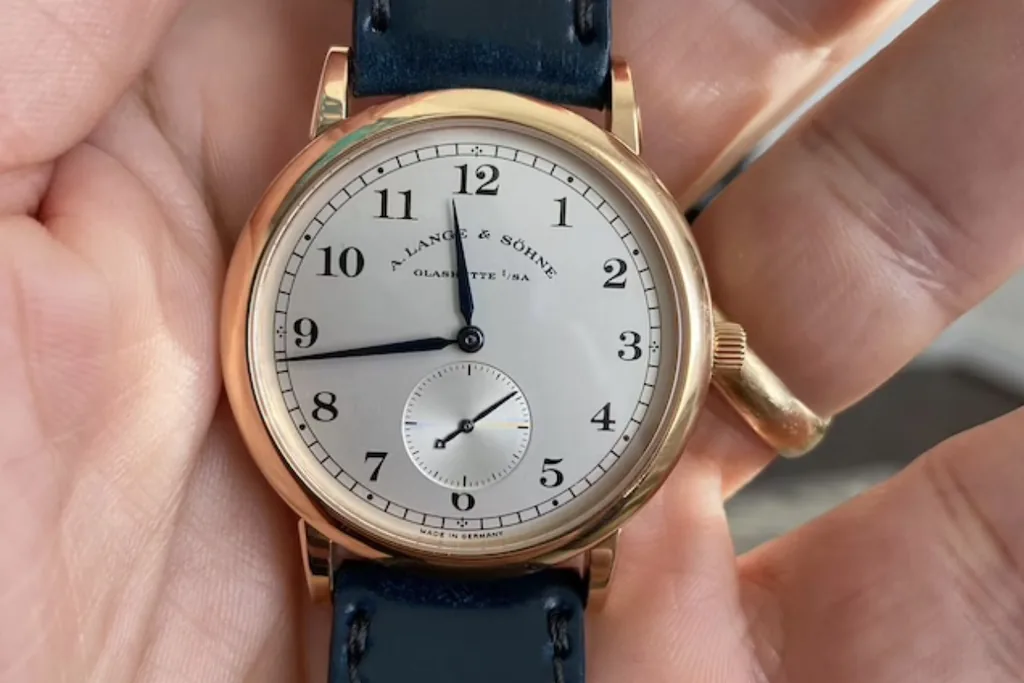 A dress watch on a navy leather strap, held in an open palm