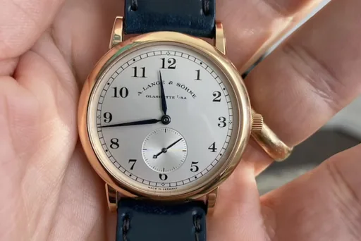 A dress watch on a navy leather strap, held in an open palm